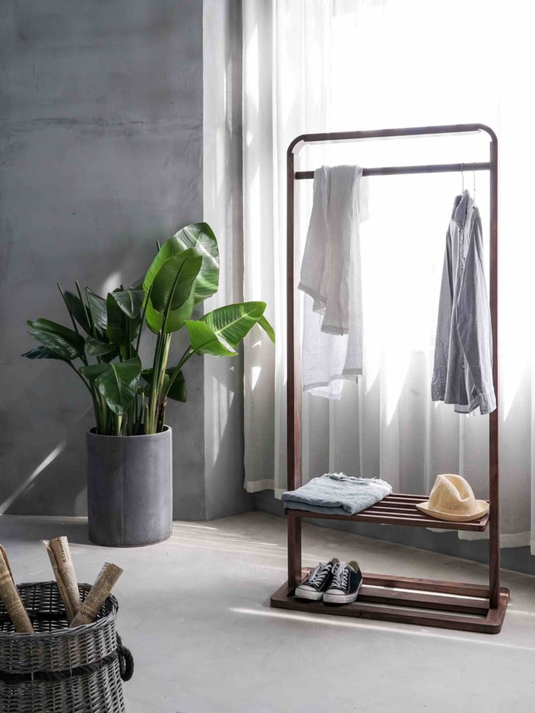 Minimalist wardrobe hung on clothes rail with grey walls and large banana plant from a blog post about How to Simplify Your Closet by Chelsey Home