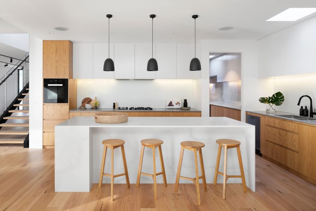 Modern Minimalist Kitchen Design with Four Wooden Stools against a White Kitchen Island