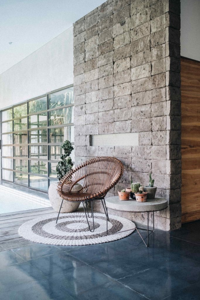 Image of a rattan chair against an exposed stone wall from a blog post "Interior Design Tips for Airbnbs" by online interior designer Chelsey Home